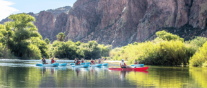 Group kayaking on a calm river with a backdrop of towering cliffs and lush greenery.