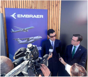 Image of two men, ABL Aviation CEO Ali Ben Lmadani and Arjan Meijer, President and CEO of Embraer Commercial Aviation, speaking into reporter microphones while standing near a poster that depicts the Embraer E2 jets.