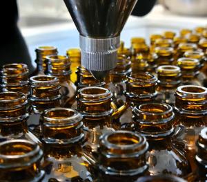 close up image of a clustered group of amber bottles with an oil filler hovering over one and pouring oil into it