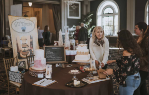 Vendor from GT Treats displays a wedding cake and dessert options, interacting with attendees at the Ultimate Wedding Expo.