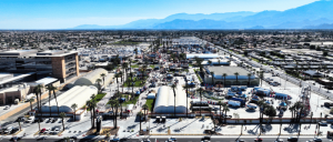 Aerial view of a bustling city street fair with tents and mountains in the background.