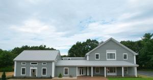 Front of Chilton Furniture's Scarborough, Maine location. A large, gray building with many windows and a flag, in front of green trees and a blue sky