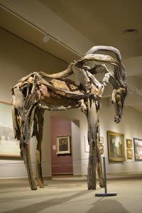 Abstract sculpture of horse, standing with its head looking at the ground, modeled from weathered branches which are cast in bronze, re-assembled, and patinaed, resembling the original wood.