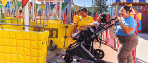 People at an amusement park with a yellow ride and a stroller visible.