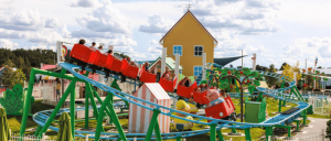 Red roller coaster in motion at a vibrant amusement park with a blue sky.