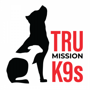 Tru Mission K9s logo featuring bold red and white text with a silhouette of a dog in profile. The words 'Tru Mission K9' are stacked, with 'Tru Mission' in white and 'K9' in bold red, against a black background. The logo represents the organization’s dedi