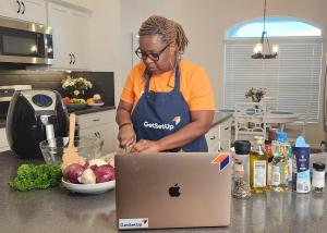 Woman cooking in front of her laptop as she is being filmed.