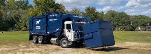 A blue front-load dumpster securely loaded onto a dumpster truck, positioned for delivery to a designated site.