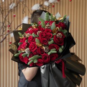 A luxurious bouquet of vibrant red roses accented with pinecones, evergreen sprigs, and gold leaves, elegantly wrapped for the festive season