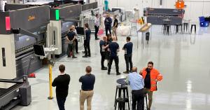 A spacious manufacturing floor with a group of workers gathered around cnc machinery, discussing operations and production.