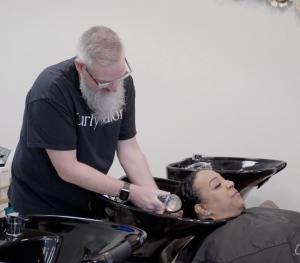 1. A woman sits in a salon chair while a man expertly washes her hair.