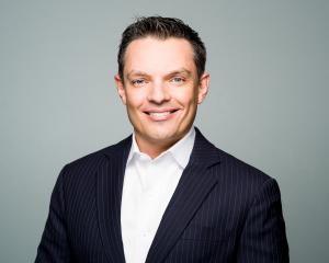 Man in coat, white shirt, no tie smiling at camera