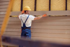 A male construction worker installing siding on a cabin.