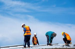 Construction workers wearing safety harnesses inspect and assemble a new roof with precision and safety.