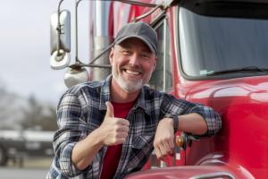 Truck driver standing next to their semi-truck, wearing a confident expression, ready for the road.