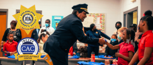 A uniformed officer from the Philadelphia Sheriff's Office shakes hands with a young student in a classroom, surrounded by children and adults, with the IBCCES Certified Autism Center™ and Philadelphia Sheriff's Office badges displayed.