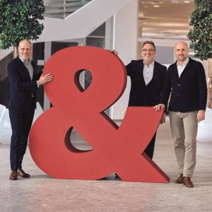 TGW Logistics' global management team standing near a large & sign, representing the new rebranding and promise of "it's possible"
