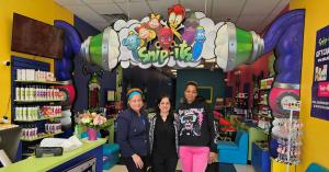 3 women standing underneath a character arch in a brightly colored hair salon.