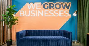 A blue velvet couch with a orange wall that reads "We Grow Businesses"