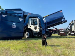 A new blue Top Dog Waste Solutions Pickup truck parked on a green lawn, with a black dog in the foreground, symbolizing efficient and reliable trash pickup solutions.