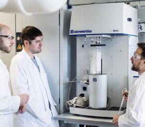 Three scientists in labcoats surround a Micromeritics 3Flex high performance gas adsorption system in a laboratory.