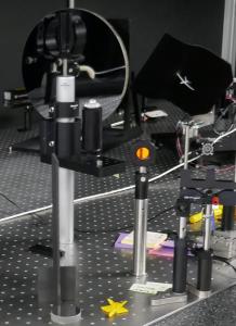 The range-in-a-box (RIAB) at Naval Postgraduate School (NPS) has a large parabolic mirror and other optical components, a 3D-printed miniature model of a drone is mounted on a gimble.