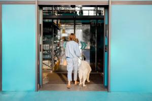 A wWoman with her dog enters a store through a green automatic door