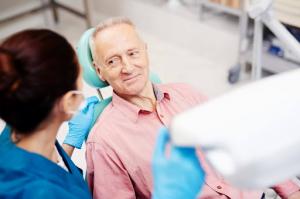 Back view of a female dentist discussing an oral cancer screening with a senior male patient seated in a dental chair.