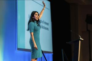 Henna Pryor on a stage in a blue dress with her hand raised