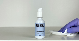 A bottle of PureGel™ shown with a clinician's hand wearing a nitrile glove, holding gauze.