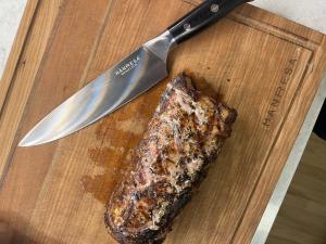 German chef pro knife sits on cherry butcher block with a grilled pork tenderloin