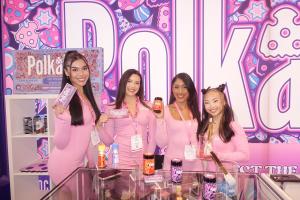 Four HQ Branding Co. brand ambassadors in pink pose at the Polka Dot booth at Expo West, holding product samples against a vibrant, branded backdrop