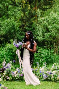 Bride long dark hair with blue floral bouquet with ribbon surrounding by blue flowers on grass