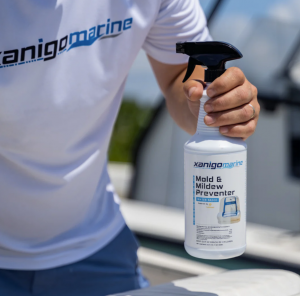 A person holding a bottle of Xanigo Marine Mold & Mildew Preventer while detailing a boat, emphasizing easy application and surface protection.