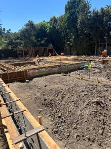 Workers in orange safety gear build wooden framing for a concrete ADU foundation surrounded by trees in Los Angeles County.