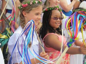 Children in festive dress, holding ribbon sticks, at a parade
