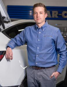 A headshot of Justin Kundrat in front of a vehicle in a collision repair facility.