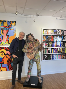 Artist Steve Joester stands in art gallery next to a sculpture of Bob Marley