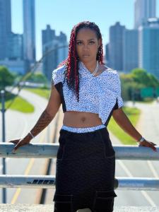 Ray Gifted Keys stands confidently on an overpass with the city skyline behind her, wearing a bold two piece and exuding street elegance.