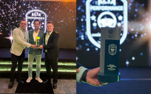 A foto apresenta a distinção atribuída à empresa Grand Lakes Veículos pelo segundo ano consecutivo, além do momento da entrega do prémio, com três homens de traje a cumprimentar-se num palco bem iluminado.