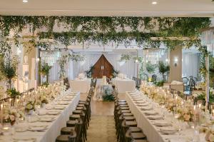 Elegant wedding reception setup at Vineyards Country Club featuring long candlelit tables, lush greenery, floral centerpieces, and sparkling chandeliers in a sophisticated indoor venue.