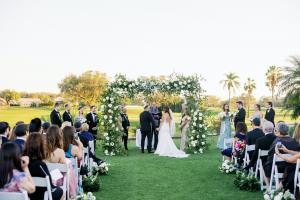 Outdoor wedding ceremony at Vineyards Country Club with a sophisticated floral arch, manicured lawns and palm trees framing the scenic golf course backdrop.