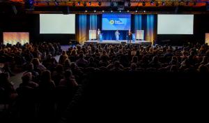 Full room of conference attendees watching a presentation on the main stage