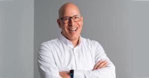 Michael Maloney, founder of Brand Force 5, smiling with arms folded in his design studio, representing the human side of design in an AI-driven world.