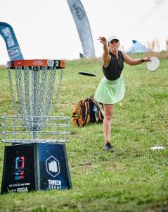 A disc golfer throwing a disc into a basket branded with the TriMech Group logo