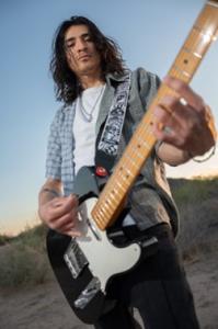 Photo of Adrian Thomas holding his guitar, as the lead singer for the Arizona Native Alt-Rock Band, ONE WAY SKY