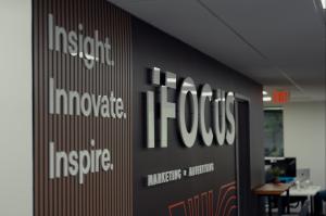 Interior office wall at iFocus Marketing featuring modern signage with the words “Insight. Innovate. Inspire.” on a wood-panel design, alongside a large 3D company logo reading “iFOCUS Marketing + Advertising” on a dark accent wall.