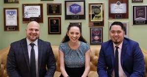 Ryan Reppucci, Katelyn Morgan, and Jonathan Roeder sitting together on a couch from left to right, smiling in a relaxed law office setting.