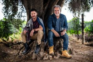 Marcelo Pelleriti and Miguel Priore seated under an olive tree at Los Pioneros Vineyard in Mendoza, holding glasses of Pelleriti Priore wine.