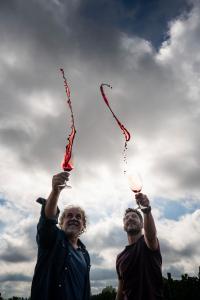 arcelo Pelleriti and Miguel Priore raise their glasses of red wine in a celebratory toast, with wine flying through the air under a cloudy sky at Los Pioneros Vineyard